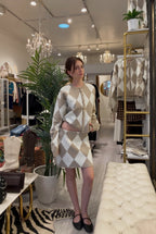 Woman wearing a cozy beige and white argyle knit skirt and cardigan set in a stylish women's clothing boutique.