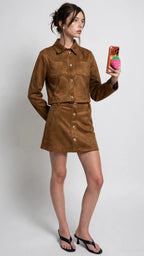 Woman wearing a camel mini skirt with gold buttons and matching jacket holding a phone taking a selfie in women's clothing