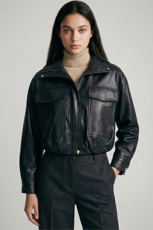 Woman wearing a black cropped vegan leather jacket with front pockets and gold hardware over a beige turtleneck.