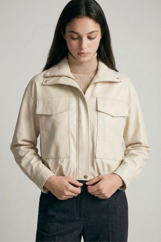 Woman wearing a cream cropped vegan leather jacket with large front pockets and gold hardware over a tan turtleneck.
