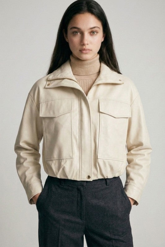 Woman wearing a cream cropped jacket with large front pockets and a beige turtleneck sweater underneath.