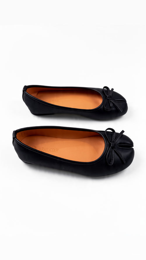 Pair of black ballet flats with bow details and orange lining on a white background