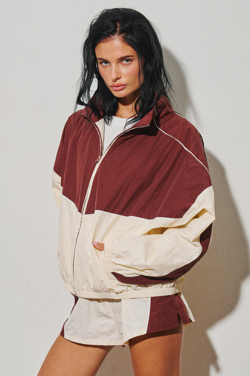 Woman wearing a burgundy and cream colorblock windbreaker jacket with a zip front