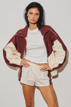 Woman wearing a burgundy and cream colorblock zip jacket with a white top and shorts