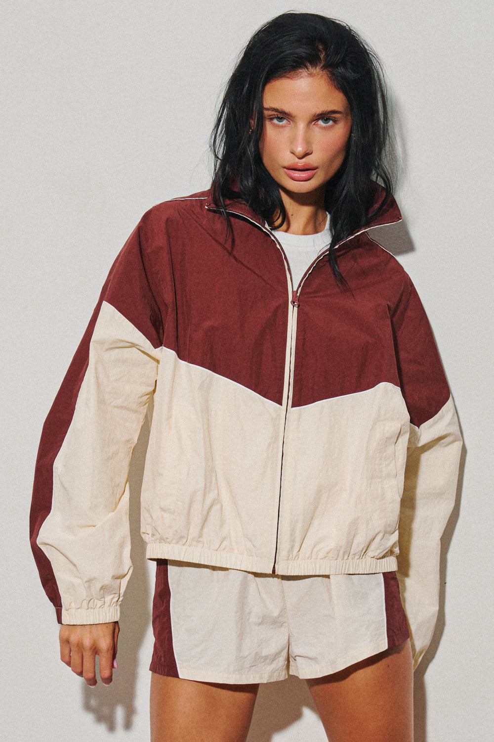 Woman wearing a burgundy and cream colorblock zip up windbreaker jacket