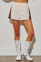Woman wearing cream colorblock nylon shorts with burgundy side panels and white sneakers
