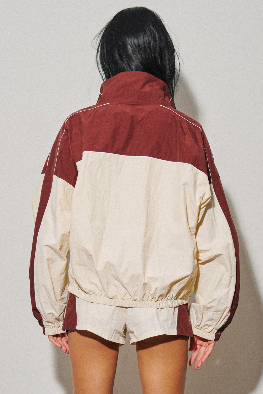 Back view of a woman wearing a red and cream colorblock nylon windbreaker jacket