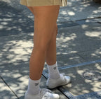 Woman wearing white statement socks and white sneakers standing on sunlit urban pavement