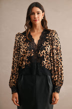 Woman wearing leopard print blouse with black lace trim and long sleeves in a neutral background.