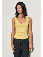 Woman wearing a yellow scoop neck tank with lace trim paired with dark denim jeans in a bright setting