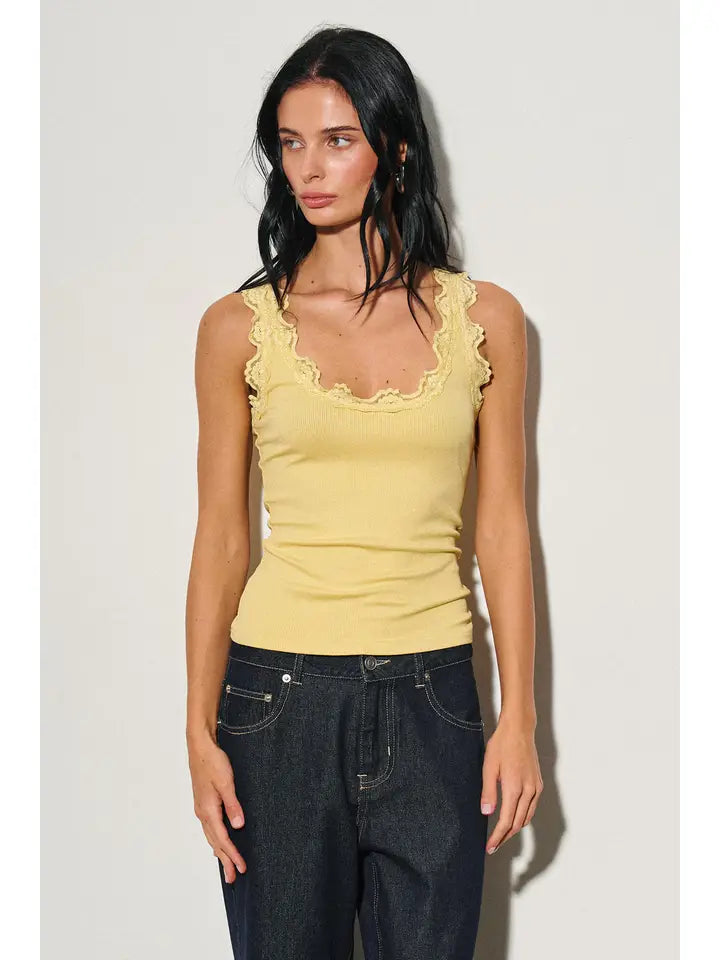 Woman wearing a yellow scoop neck tank with lace trim paired with dark denim jeans in a bright setting