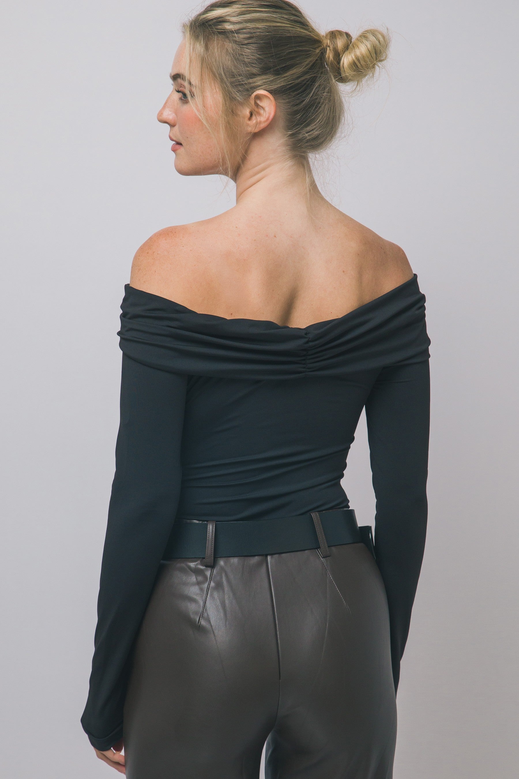 Woman wearing off-shoulder long-sleeve black top paired with high-waisted dark leather pants in women's clothing style