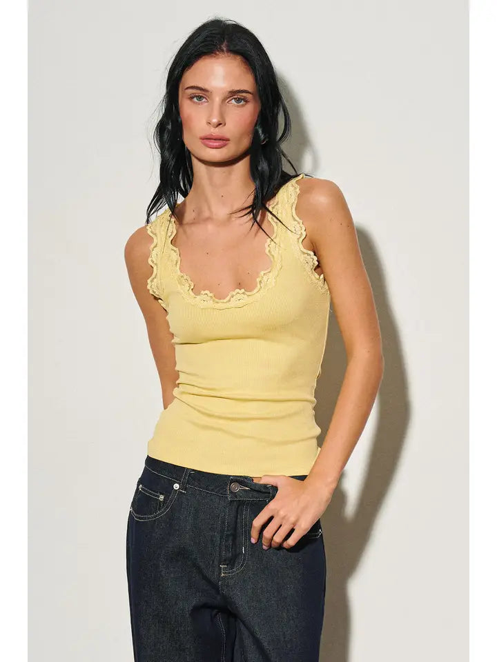Woman wearing a fitted yellow lace-trimmed tank top paired with dark denim jeans in a fashion photoshoot.