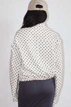 Woman wearing a Polkadots Funnel Jacket with black polka dots on white fabric, paired with a beige cap, viewed from the back.