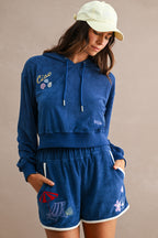 Woman wearing a blue terry cloth hoodie and shorts with beach-inspired embroidered designs and contrast trim accents