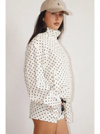 Woman wearing a white jacket with black polka dots, a high funnel neck, and elastic hem, paired with matching shorts.
