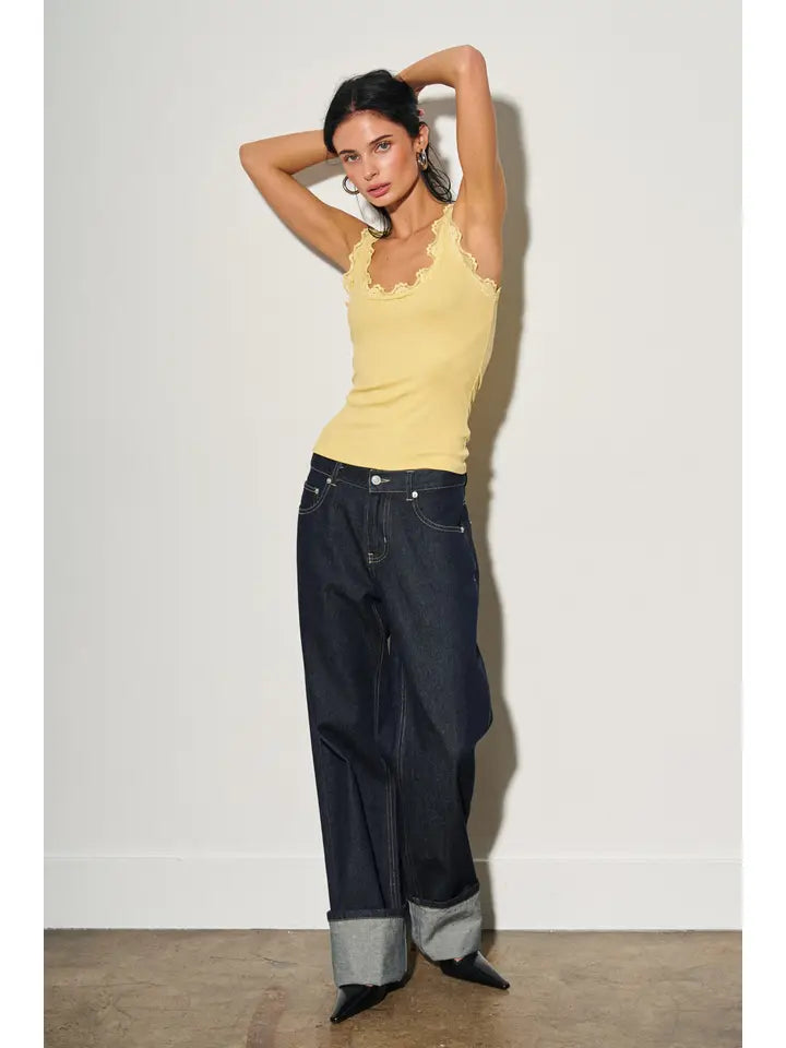 Woman wearing a yellow lace-trimmed scoop neck tank top paired with dark wide-leg cuffed jeans and black heels