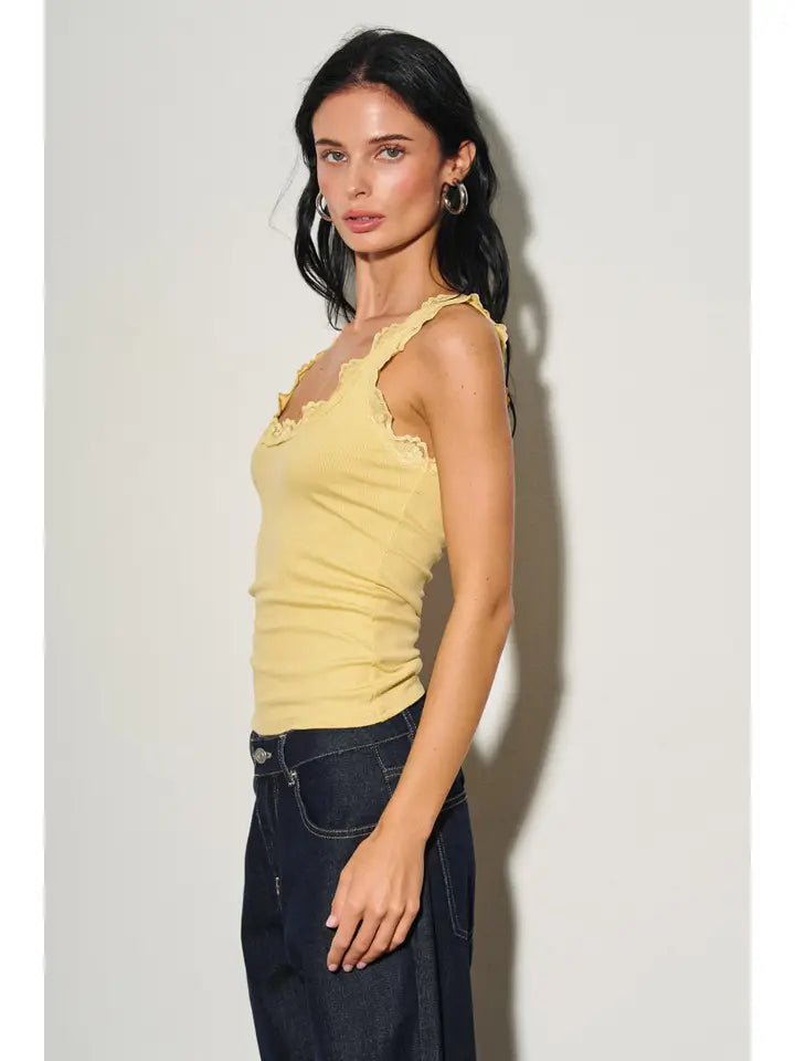 Woman wearing a fitted yellow lace-trimmed tank top paired with dark denim jeans in a studio setting