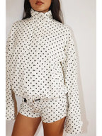 Woman wearing a white Polkadots Funnel Jacket with black polka dots, featuring a high funnel neck and long sleeves, paired with matching polka dot shorts.