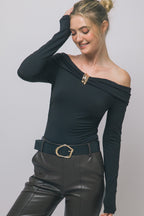 Woman wearing black long-sleeve bodysuit with draped neckline and gold buckle paired with dark pants and belt.