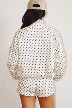 Rear view of a person wearing a white Polkadots Funnel Jacket with black dots, paired with matching shorts and a beige cap.