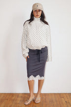 Woman wearing a polka dot zip-up jacket with high neckline paired with a navy skirt featuring lace trim at the hem