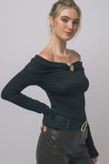 Woman wearing black long-sleeve top with folded neckline and gold buckle, paired with dark pants and belt