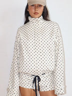 Woman wearing a white zip-up jacket with black polka dots and matching shorts, styled with a beige cap.