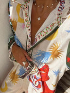 Woman in colorful sun and abstract print shirt with layered necklaces and rings on hand