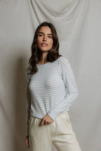 Woman wearing a white and light blue striped long sleeve top paired with cream pants against a beige backdrop