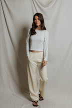 Woman wearing a white striped long sleeve crop top and cream wide-leg pants in a neutral studio setting