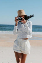 Woman wearing a striped long sleeve shirt and bucket hat taking photo on a sunny beach in women's clothing