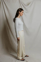 Woman wearing a fitted striped long sleeve top and loose cream pants standing against a draped fabric backdrop