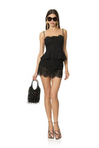 Woman wearing black lace peplum top and matching shorts with sunglasses and high-heeled shoes holding a fringe handbag