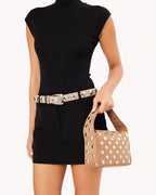 Woman in black dress holding a tan faux leather bag with silver stud accents matching her belt