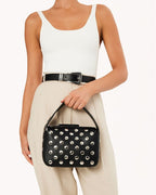 Woman wearing white tank top and beige pants holding black faux leather bag with silver studs