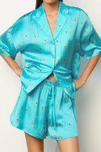 Woman wearing shiny turquoise lounge top and matching shorts with swimmer pattern in relaxed fit style