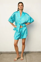 Woman wearing a vibrant turquoise lounge top and matching shorts in lightweight fabric with subtle print details.