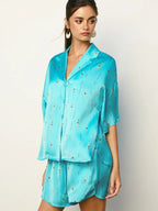 Woman wearing a loose fit shiny turquoise top with small swimmer print and matching shorts in women’s clothing style