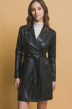 Woman wearing a black vegan leather jacket with button closure and waist belt over a white turtleneck sweater