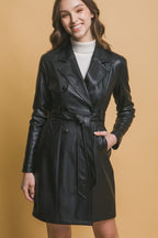 Woman wearing a black vegan leather jacket with button closure, waist belt, and side pockets over a white turtleneck sweater