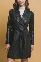 Woman wearing a black vegan leather belted jacket over a white turtleneck against a beige background