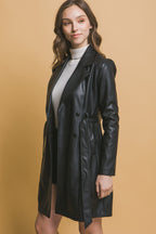 Woman wearing a black vegan leather jacket with button closure and detachable waist belt over a white turtleneck