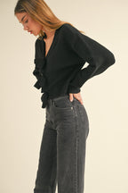 Woman wearing a black knit sweater top with bow details down the front paired with high-waisted dark jeans.