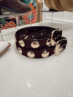 Black women's belt with large silver studs and a silver buckle displayed on a white surface in a fashion store.