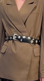 Black leather belt with silver oval studs and buckle styled over a tan women's blazer jacket