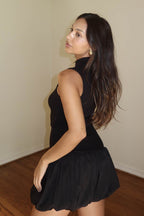 Woman wearing a sleeveless black bubble mini dress with ribbed texture and long loose hair in indoor setting