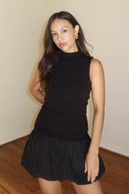 Woman wearing a sleeveless black ribbed top paired with a black bubble mini skirt in a casual indoor setting.