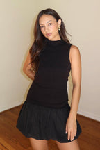Woman wearing sleeveless black ribbed top and black bubble mini skirt standing indoors