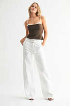 Woman wearing high-rise belted wide leg white pants paired with a brown and beige sleeveless top in studio.